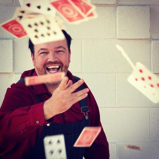 A playful and energetic moment as Matt Donnelly tosses playing cards into the air, embodying the joy and wonder of magic.